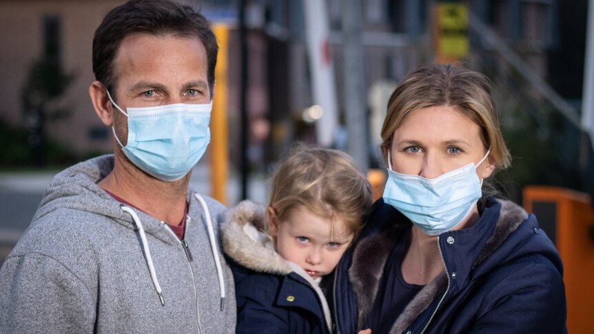 A man and woman wear masks while holding a toddler.