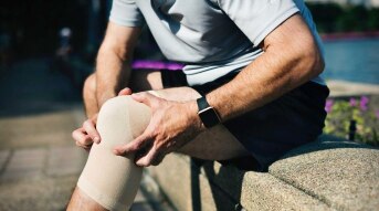 Man holding sitting down holding his knee which has a brace on it.