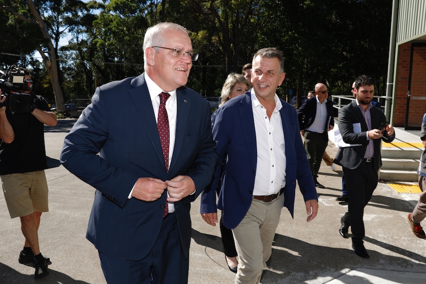 Scott Morrison wearing a blue suit and red tie walks alongside Andrew Constance outside. 