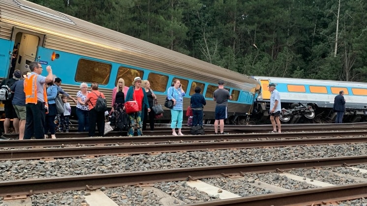 A train derailed and one carriage on its side with passengers standing outside