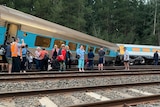 A train derailed and one carriage on its side with passengers standing outside
