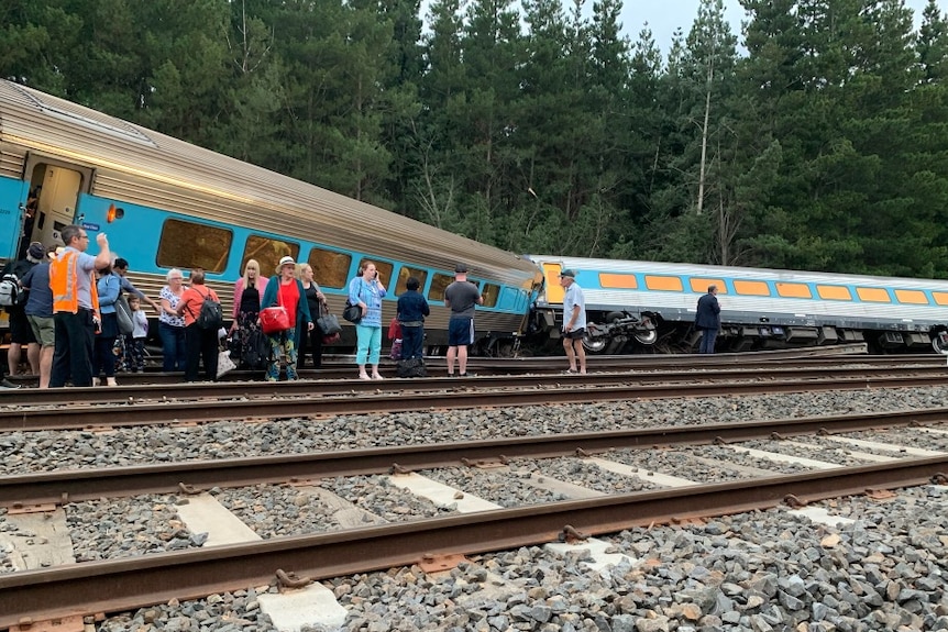 A train derailed and one carriage on its side with passengers standing outside