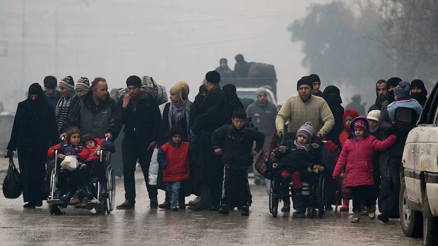 A group of civilians, including women and children, walk down run-down streets of Aleppo.