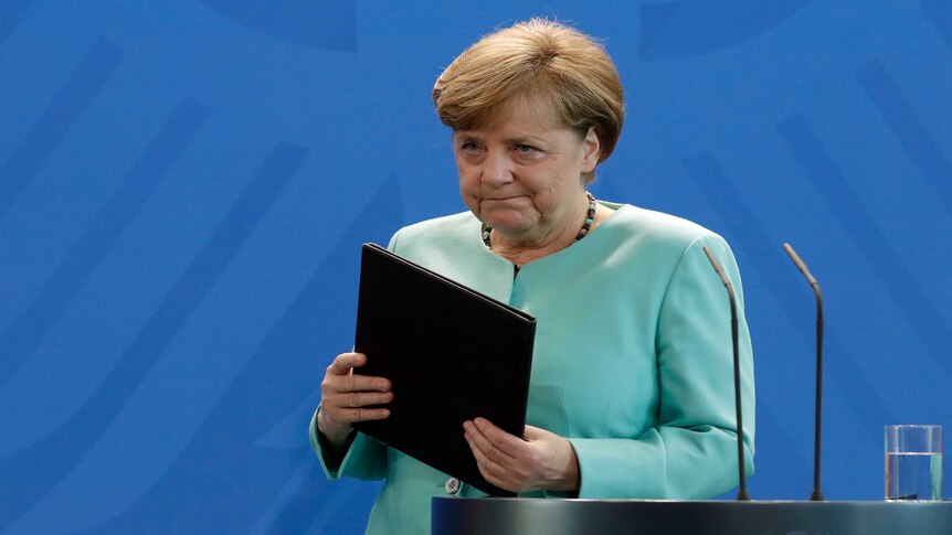German Chancellor Angela Merkel leaves the podium with a black folder, wearing an aquamarine pantsuit