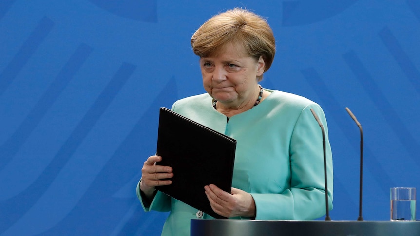 German Chancellor Angela Merkel leaves the podium with a black folder, wearing an aquamarine pantsuit