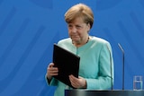 German Chancellor Angela Merkel leaves the podium with a black folder, wearing an aquamarine pantsuit