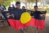 Two young indigenous boys told an Aboriginal flag. 