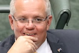Scott Morrison grins while resting a hand on his chin. The back of Peter Dutton's head is visible.