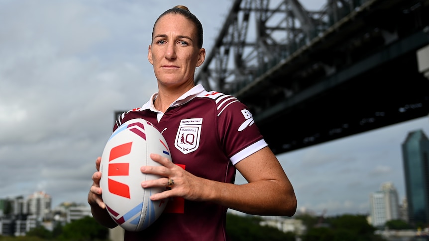 Female State of Origin player Ali Brigginshaw, wearing a Maroon jersey holding a football in front of a bridge
