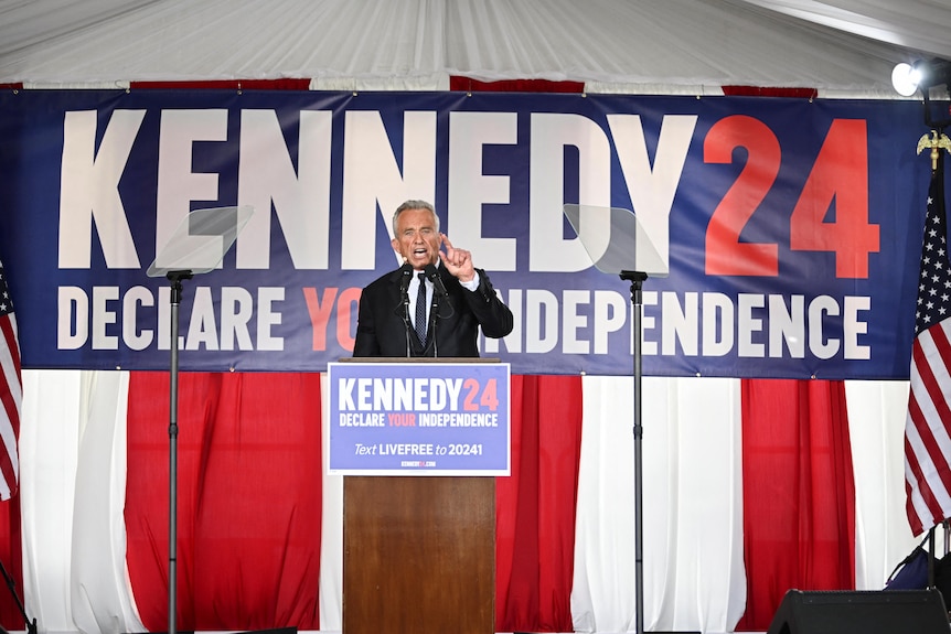 RFK Jr stands at a podium in front of a sign that reads 'Kennedy 24 Declare Your Independence'