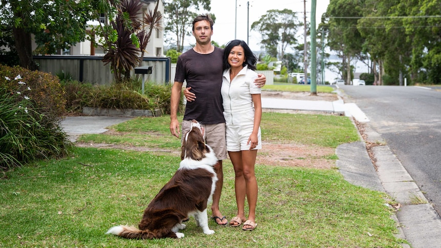 Jason Cullen and Tansiri Harnwattanachai stand out the front of their house with their dog at their feet.