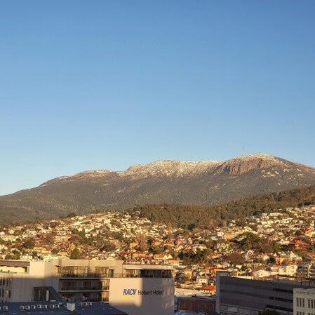 A snow-capped Mt Wellington/kunanyi with foothills and Hobart city in the foreground.