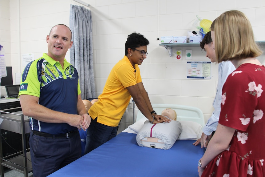 A group of people standing around a hospital bed with a medical dummy on the bed