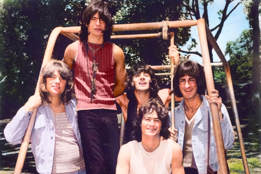 Colour photo of five men leaning on outdoor play gym, taken in 1970s