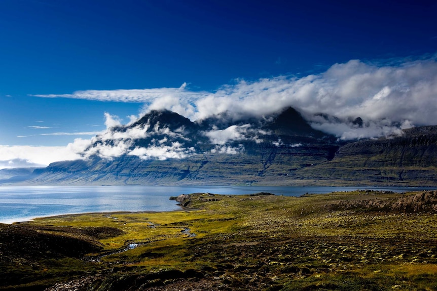 Wide landscape shot of a sun-drenched plain leading down to water with mountains in the background.