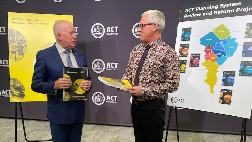 Two men holding pieces of paper standing in front of easels that say ACT Government. 