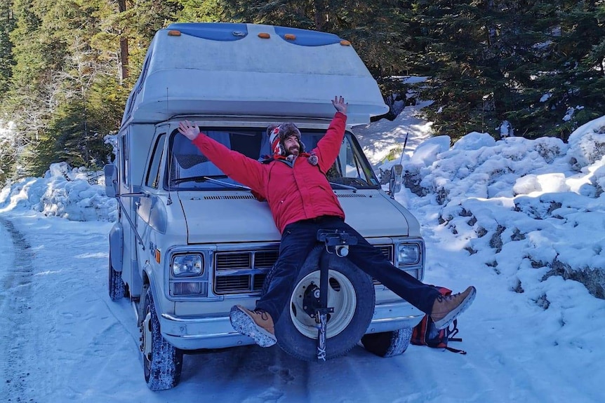 Ben Richards lies on the front of his campervan on a snowy road