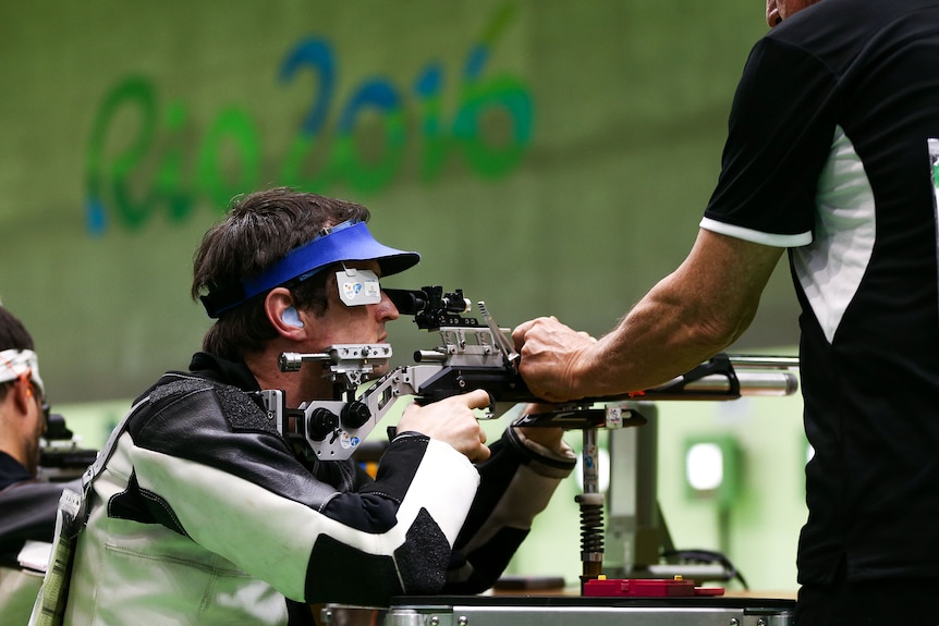 A Paralympic shooter aims his air rifle using a shooting stand.