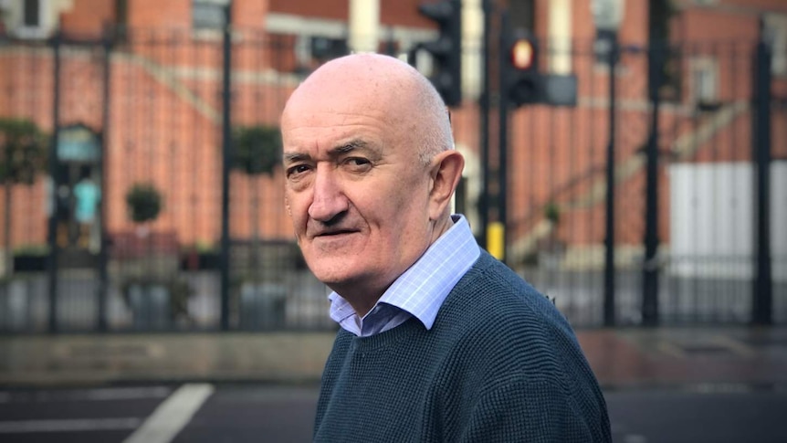 An older man stares intensely at the camera on an street in the UK.