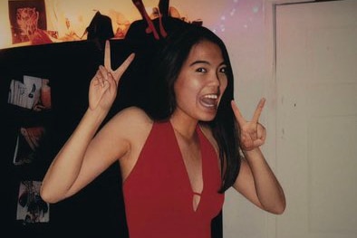 A photo of a smiling girl in a red dress, with her hands up in peace signs with warped fingers, her left shoulder raised oddly
