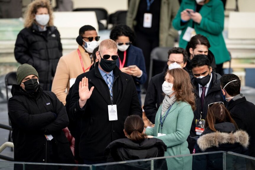 Some people stand with masks on as one person takes an oath