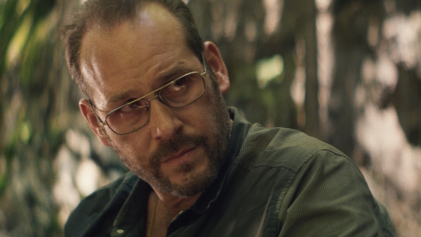 Dean Imperial, a middle aged man in aviator glasses in a forest looking tired, in the film Lapsis