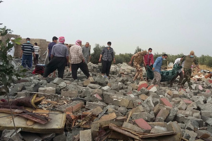 A dozen men wearing surgical masks look through rubble after a coalition airstrike in Fadhiliya near Mosul, Iraq.