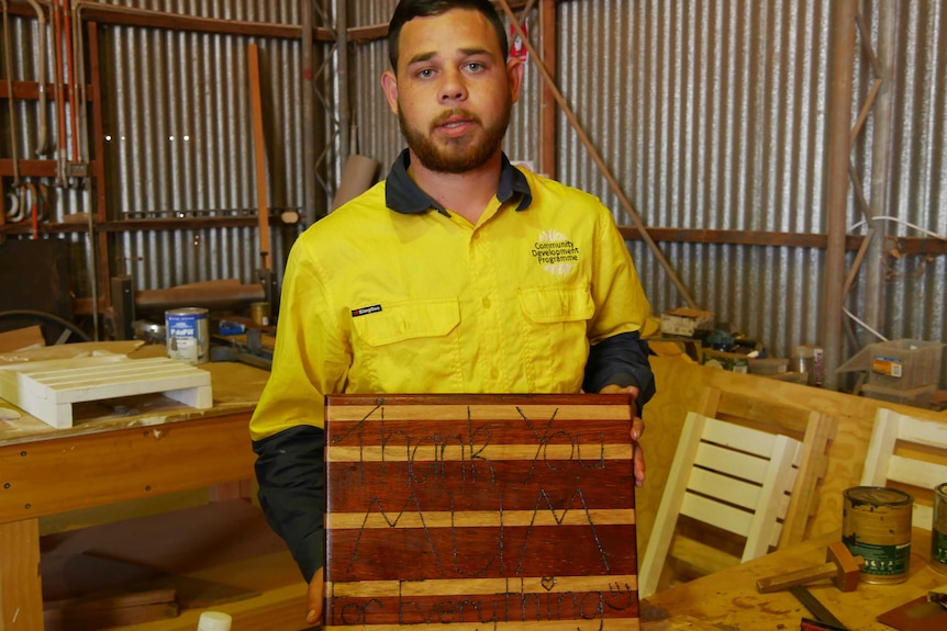Young Indigenous man holding a wooden chopping board engraved with the words 'Thank You Mum for Everything'