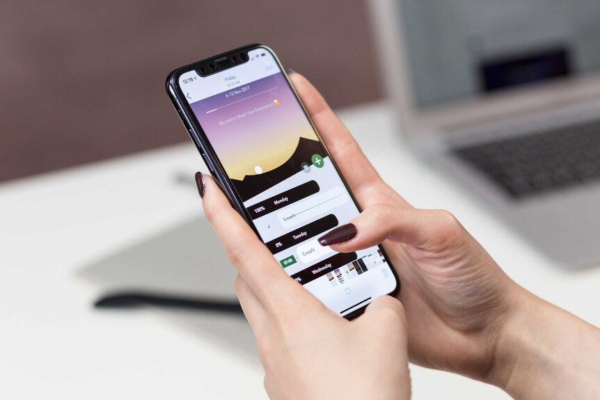 A woman holds an iPhone X with two hands and taps on her calendar app.