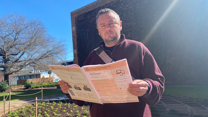 A man holds the 2021 census paper and is frowning 