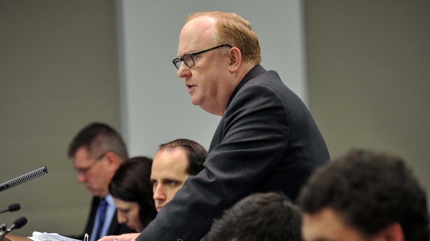 Geoffrey Watson stands at a lectern and speaks to a room of people