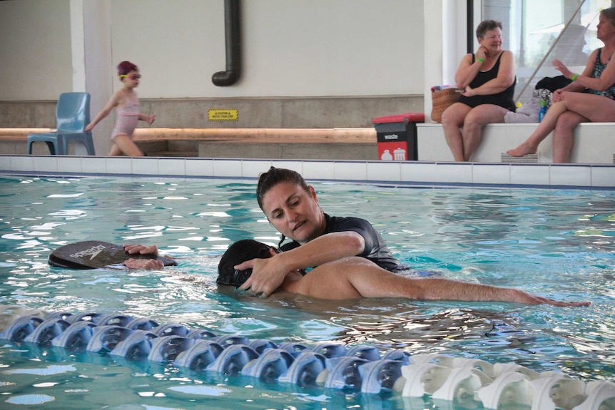 A swim instructor helping somebody in the water.