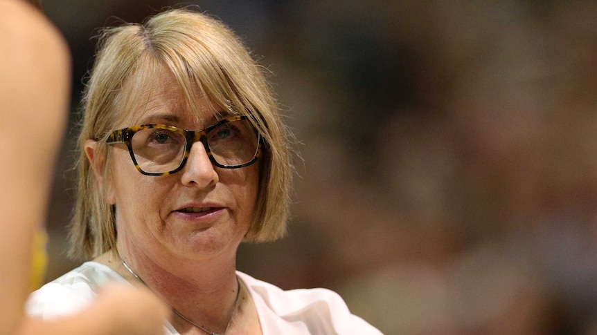 Lisa Alexander pulls up her sleeve of her white top as she talks to a netball player wearing a yellow dress