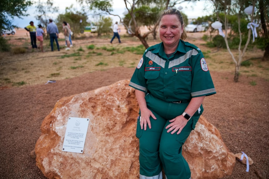 A woman in a paramedic uniform sits on a rock that has a plaque on it