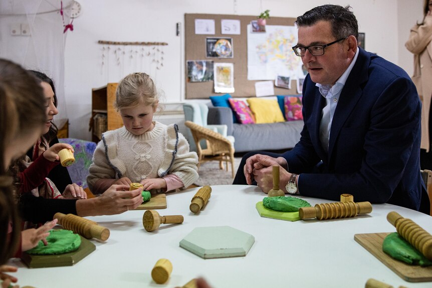 Daniel Andrews sits at a table with children playing with toys
