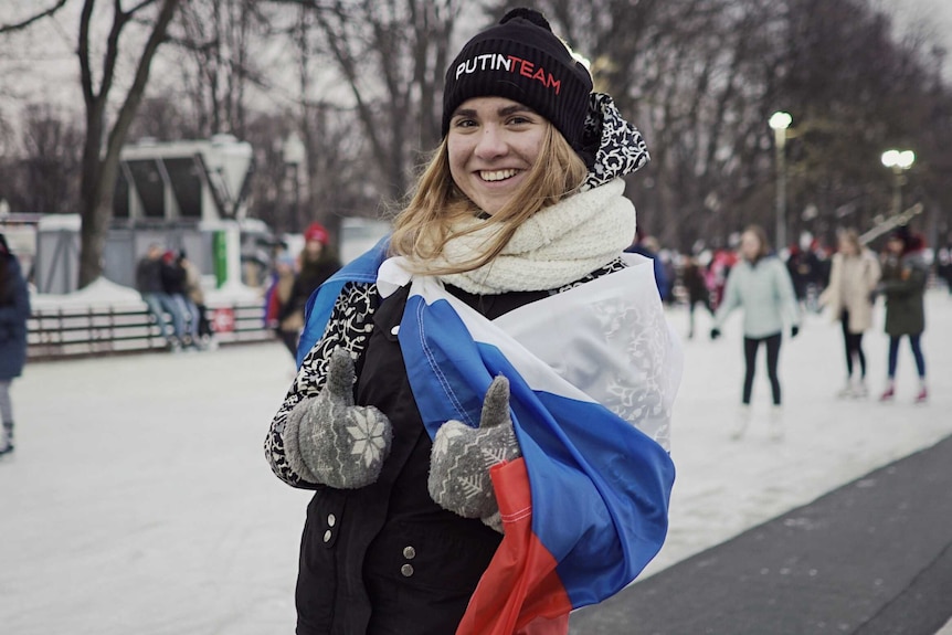 Alexandra Baranova wears a russian flag over her shoulders and a putin team beanie