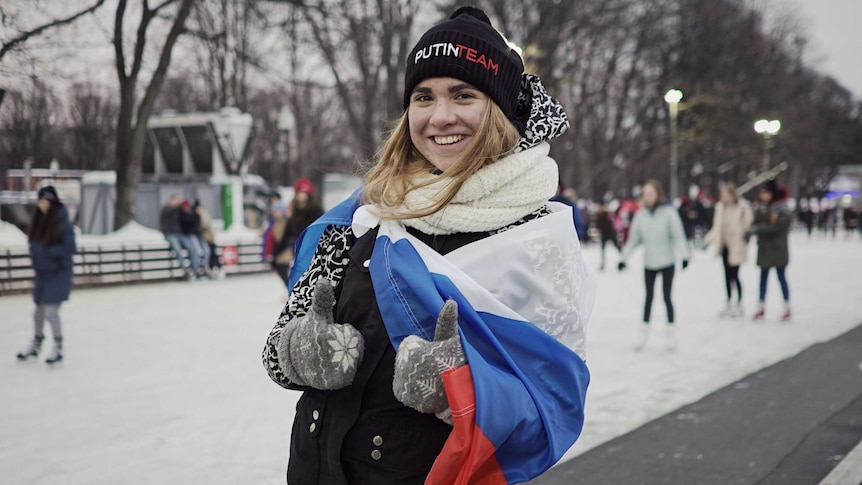 Alexandra Baranova wears a russian flag over her shoulders and a putin team beanie