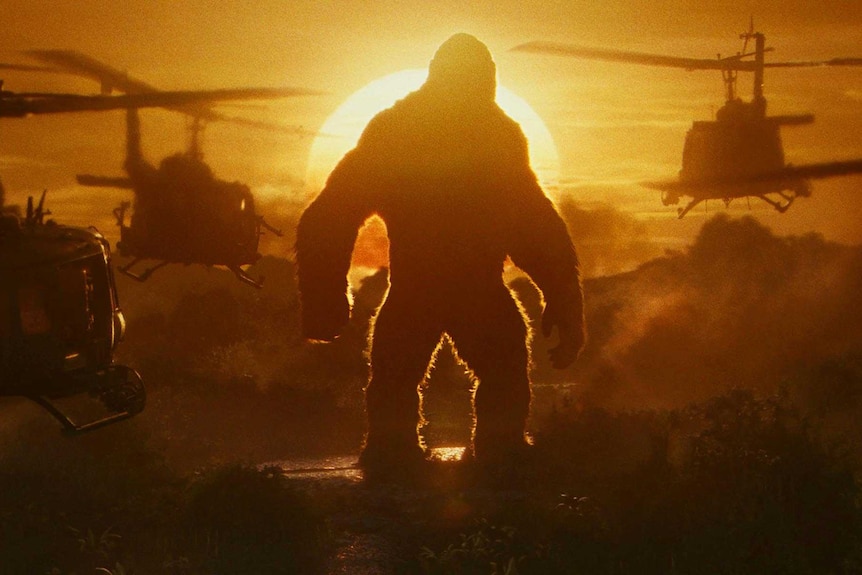 The sun sets behind Kong, surrounded by helicopters.