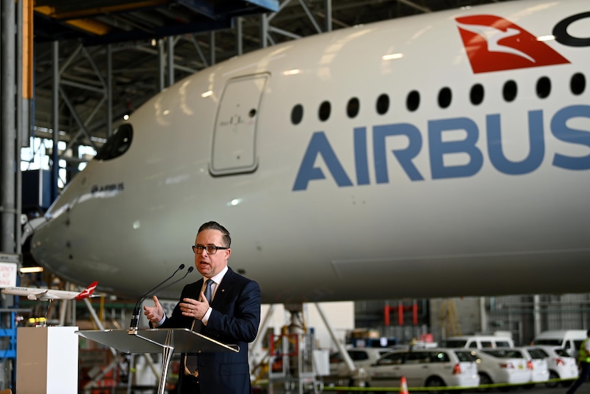 a man wearing glasses speaking in front of an airplane