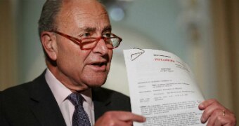 Chuck Schumer holds and points to a document that has UNCLASSIFIED printed on it in red.