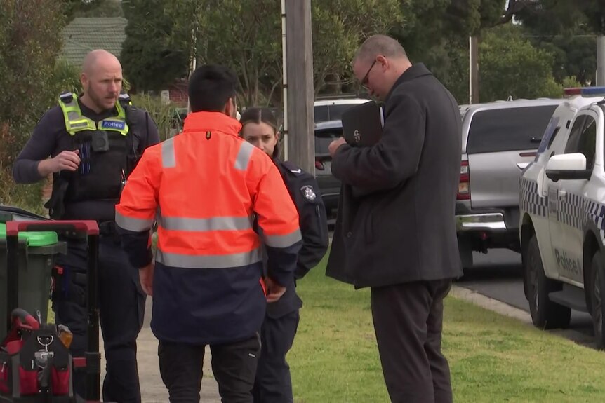 Four uniformed detectives standing in the front yard of a property.