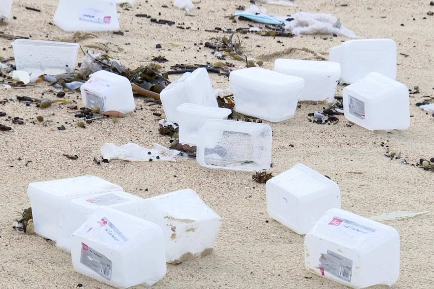 Several plastic containers scattered across sand on a beach
