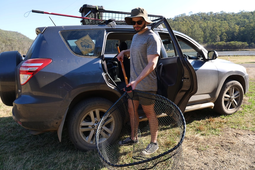 A man holding a net next to a four-wheel drive car