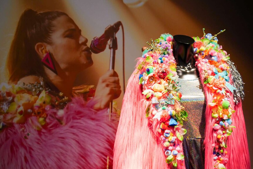 Bright pink costume in front of a photo of a lady singing.