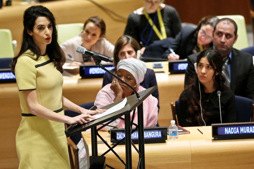 Amal Clooney speaks at podium as other people listen.