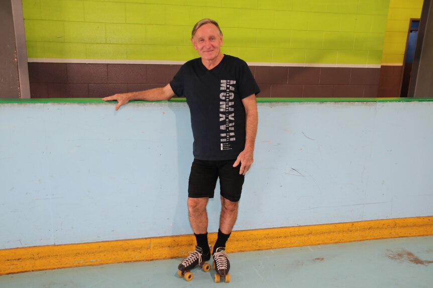 older man standing on a roller rink in a black shirt wearing rollerskates 