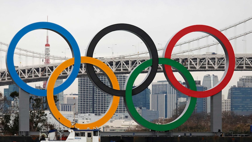 Giant versions of the five-coloured Olympic rings stand in front of a view of the city of Tokyo.