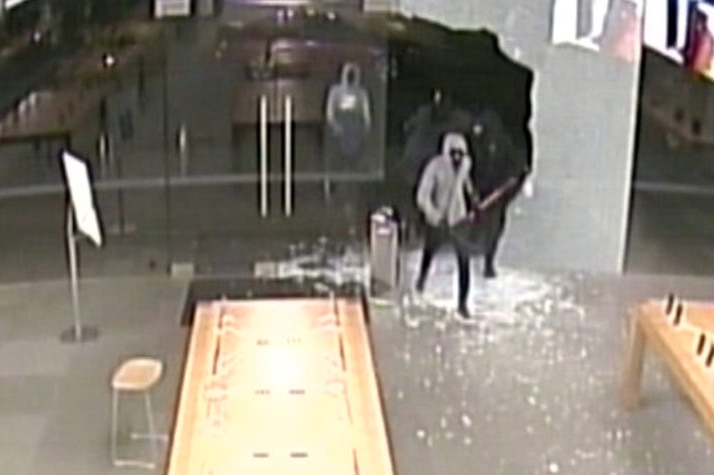 A still frame taken from CCTV footage from inside an Apple store showing thieves entering through a broken glass door.