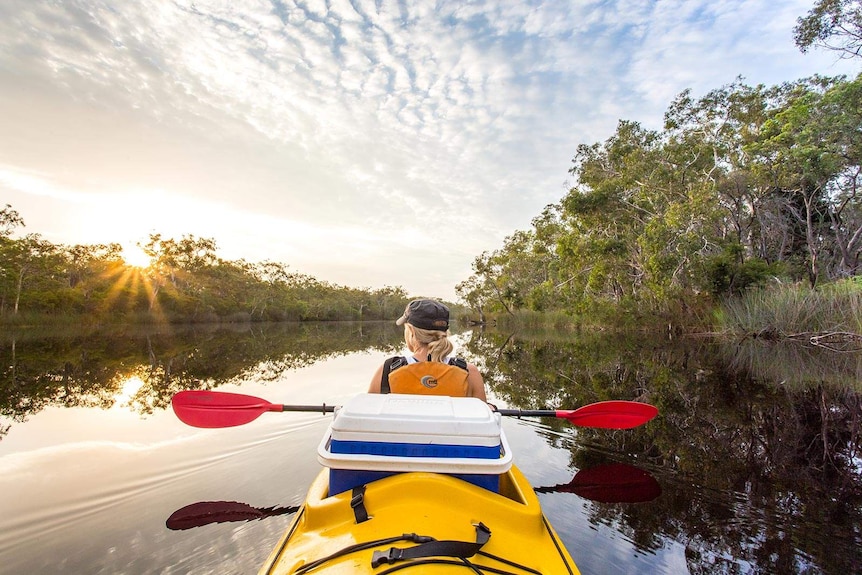 A woman paddles a canoe into the sunset.