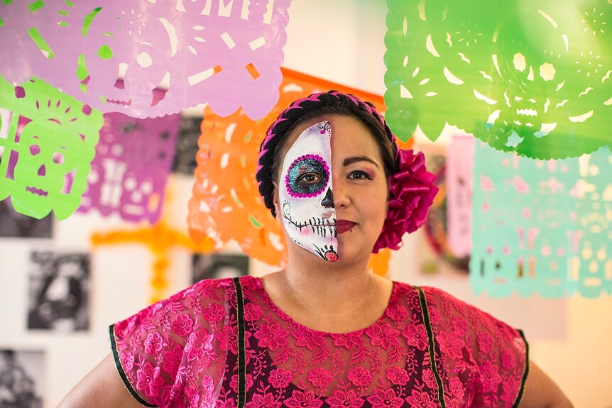 A woman with her face painted stands with a string of colourful stencils hanging around her.
